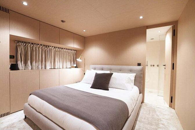 Cozy modern bedroom interior with warm wood paneling, built-in storage, queen bed dressed in white linens and gray throw, bedside lamp and a visible ensuite shower — stylish compact living space.