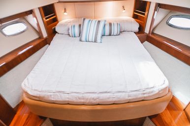 Cozy yacht cabin bedroom interior with a neatly made bed, striped accent pillows, warm varnished wood trim and oval porthole windows