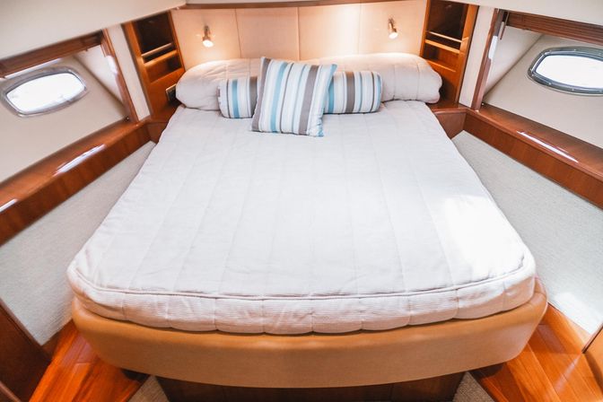 Cozy yacht cabin bedroom interior with a neatly made bed, striped accent pillows, warm varnished wood trim and oval porthole windows