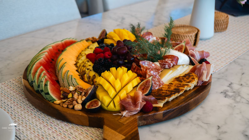 Vibrant gourmet charcuterie board on a marble countertop with sliced watermelon, cantaloupe, carved mango, pineapple, grapes, berries, figs, mixed nuts, cured meats, cheeses and grilled halloumi, perfect for entertaining.
