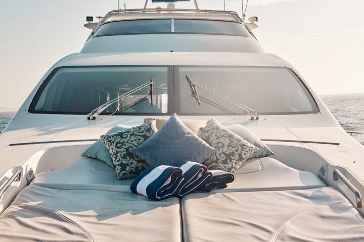 Sunlit luxury yacht bow with an inviting sunpad, decorative patterned pillows and rolled navy-striped towels, overlooking calm open sea