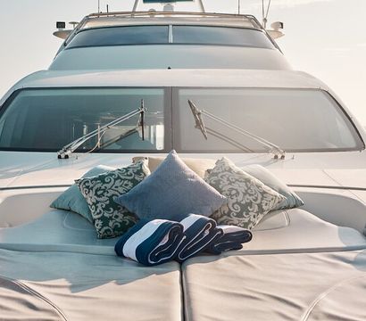 Sunlit luxury yacht bow with an inviting sunpad, decorative patterned pillows and rolled navy-striped towels, overlooking calm open sea