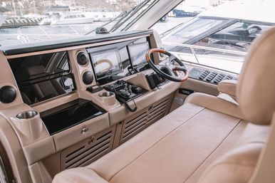 Luxury yacht helm with beige leather bench, wooden-trim steering wheel, dual navigation screens and marina views