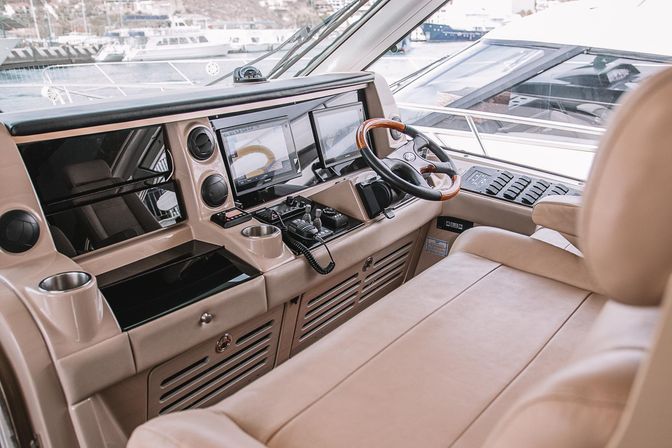 Luxury yacht helm with beige leather bench, wooden-trim steering wheel, dual navigation screens and marina views