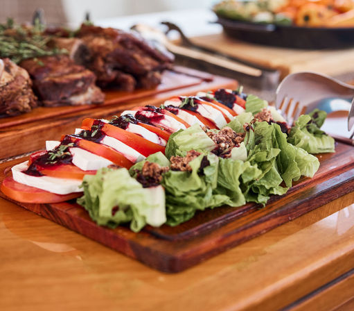 Fresh Caprese-style salad with alternating tomato and mozzarella slices, basil and balsamic glaze, crunchy nuts and lettuce arranged on a wooden serving board.
