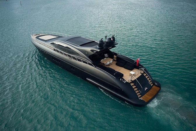 Aerial view of a sleek black luxury motor yacht gliding on turquoise water, teak rear deck with lounge seating and swim platform