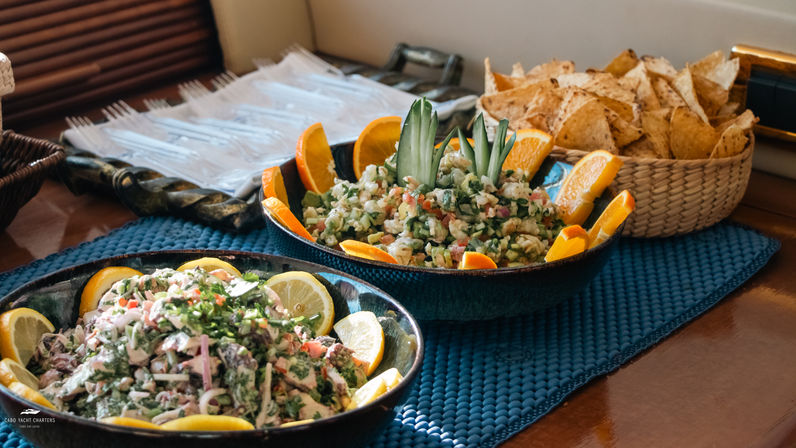 Two bowls of fresh seafood ceviche and chopped salads garnished with lemon and orange wedges, served with tortilla chips in a woven basket on a blue placemat.
