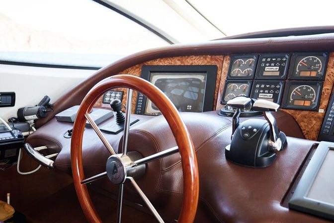 Luxury yacht helm with polished wooden steering wheel, leather-wrapped dashboard, navigation display, twin throttle controls and engine gauges
