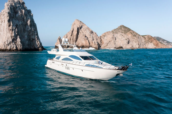 Aerial view of a luxury white yacht cruising turquoise ocean near dramatic rocky sea stacks under a clear blue sky