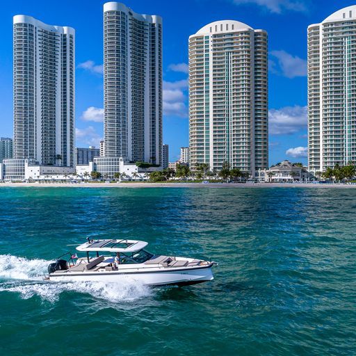 Sleek motorboat cutting through turquoise ocean in front of beachfront high-rise condo towers under a bright blue sky