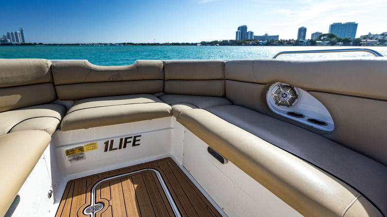 Padded beige boat seating and teak deck overlooking turquoise bay water and a distant city skyline on a sunny day.