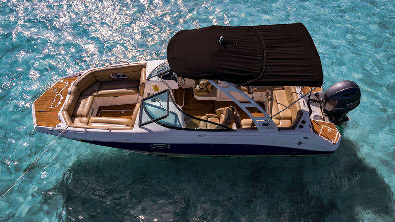 Aerial shot of a white motorboat with tan leather seating and a black bimini top anchored in sparkling turquoise tropical water.