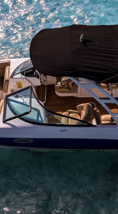Aerial shot of a white motorboat with tan leather seating and a black bimini top anchored in sparkling turquoise tropical water.