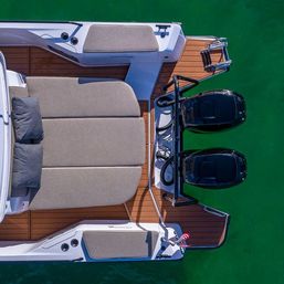 Aerial view of a modern motorboat stern with twin black outboard engines, teak swim platform and cushioned sun pad over clear green water
