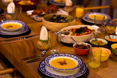 Cozy wooden dining table set for a family-style meal with blue-patterned bowls of creamy orange soup, colorful bowls of salsas and dips, a salad, drinking glasses and napkins.