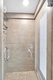 Spa-style walk-in shower with glass door and chrome handle, rainfall showerhead and beige textured tiles for a modern residential bathroom.