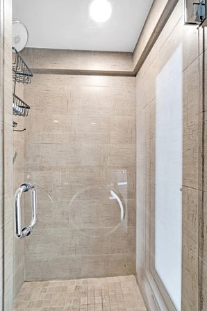Spa-style walk-in shower with glass door and chrome handle, rainfall showerhead and beige textured tiles for a modern residential bathroom.