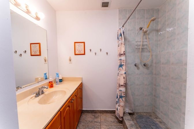 Bright residential bathroom with single-sink vanity and wood cabinets, large mirror, tiled walk-in shower with handheld showerhead and nautical starfish shower curtain.