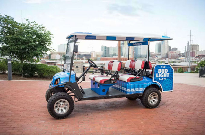 Blue promotional party golf cart with canopy and red-and-white seats parked on a brick waterfront promenade with urban skyline and river in the background.