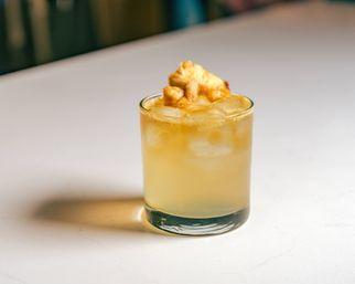 Craft tropical pineapple cocktail on ice in a lowball glass, topped with dried pineapple garnish on a white countertop