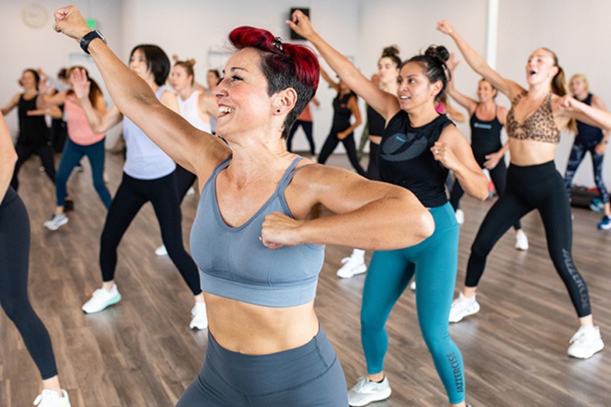Energetic group fitness class of women doing cardio dance moves in a bright indoor fitness studio with wood floors