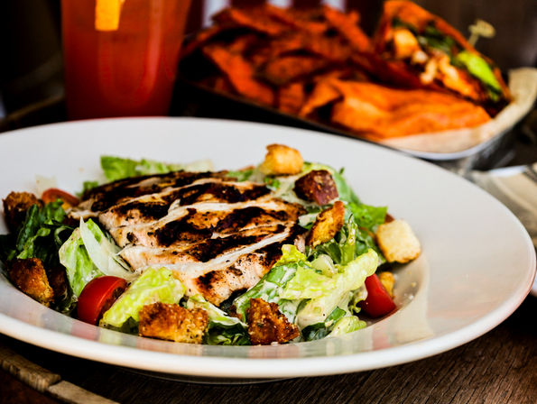 Restaurant-style grilled chicken Caesar salad with romaine, cherry tomatoes, crunchy croutons and creamy dressing, served with sweet potato fries and a cold drink