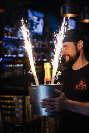 Person holding a metal ice bucket with a champagne bottle and two large lit sparklers in a dim bar — festive bottle service and celebration.