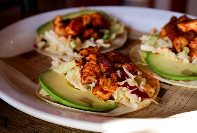 Close-up of Mexican-style grilled chicken tacos topped with avocado slices and cabbage slaw on corn tortillas on a white plate