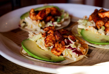 Close-up of three Mexican-style grilled chicken tacos on corn tortillas topped with avocado slices and cabbage slaw on a white plate