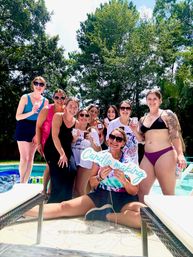 Smiling group of friends at a sunny backyard poolside candle-making party, holding mini candles and a 'Candle making' sign under tall trees.