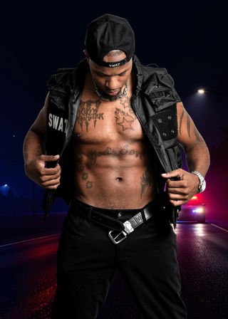 Muscular shirtless man in a black SWAT cap and tactical vest, opening his vest to show tattooed chest and abs with a chain necklace, posed on an urban night street lit by red and blue police cruiser lights.