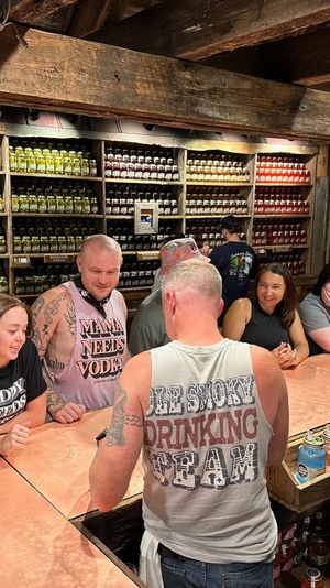 Bustling rustic tasting bar in a mountain‑town shop — people sampling colorful jarred spirits and preserves on wooden shelves beneath exposed beams