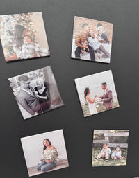 Seven square custom photo magnets on a black background showing family scenes: holiday mom with infant, parents with baby and pets, grayscale groom with older woman, wedding couple exchanging rings, pregnant woman with bouquet, and two toddlers outdoors.