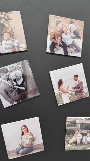 Seven square custom photo magnets on a black background showing family scenes: holiday mom with infant, parents with baby and pets, grayscale groom with older woman, wedding couple exchanging rings, pregnant woman with bouquet, and two toddlers outdoors.