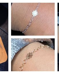 Close-up wrist jewelry detail: two delicate chain bracelets (one silver, one gold) with small textured sunburst flower charms, styled as stackable everyday accessories.