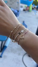 Sunlit backyard wrist with stacked dainty gold and silver bracelets featuring tiny charms and multicolored beads