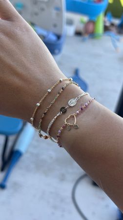 Sunlit backyard wrist with stacked dainty gold and silver bracelets featuring tiny charms and multicolored beads