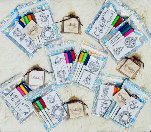 Flat-lay of holographic zip bags with mini holiday coloring cards and bright markers arranged on white faux-fur — festive kids activity kits and stocking-stuffer gift sets.