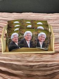 Smiling gray-haired woman portrait photo cards arranged in a wooden tray on pink textured fabric