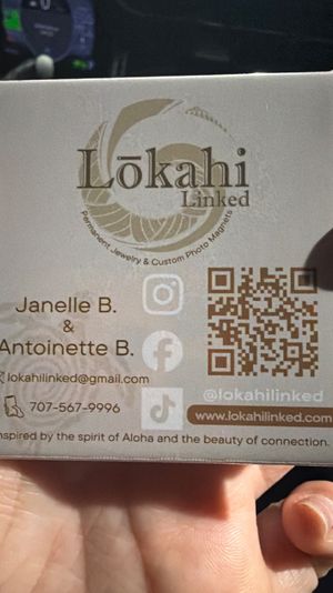 Close-up of a hand holding a small jewelry product box with a circular logo, QR code, social media icons and the tagline “Inspired by the spirit of Aloha,” suggesting Hawaii‑inspired jewelry packaging.