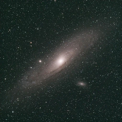 Astrophotography of the Andromeda Galaxy (M31): bright spiral core with sweeping faint arms surrounded by a dense, star-filled night sky