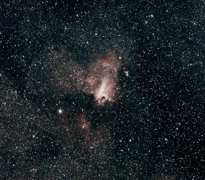 Cosmic deep-sky view: dense Milky Way star field with a pinkish emission nebula and dark dust lanes against black space.