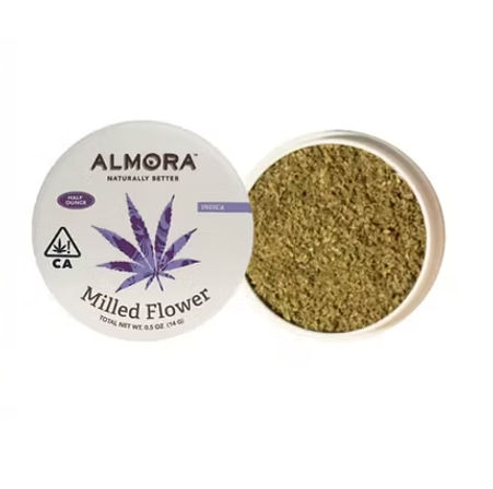 Open white tin of milled cannabis flower with a purple leaf graphic on the lid, showing finely ground green indica herb inside.