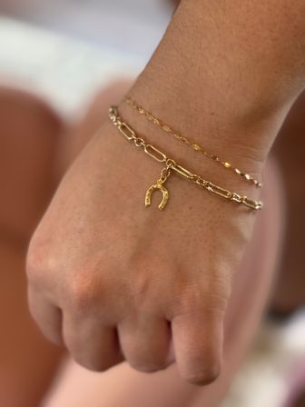 Close-up of delicate gold chain bracelets on a wrist, one featuring a tiny horseshoe charm — minimalist wrist jewelry, gold bracelet detail.