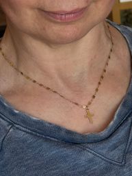Close-up of lower face and neck wearing a shiny gold cross pendant on a delicate chain over a blue-gray sweatshirt.