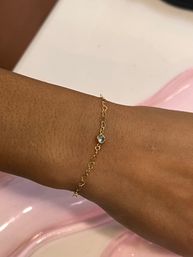 Close-up of a wrist wearing a dainty gold chain bracelet with a small bezel-set clear crystal and tiny star charm against a glossy pink background