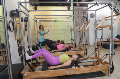 Bright modern Pilates reformer studio — instructor guiding a group of women through leg-bridge exercises on reformer machines