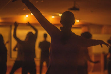 Silhouetted dancers in a warm-lit indoor studio during a lively group dance class.