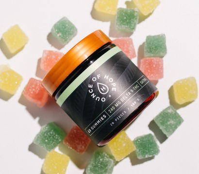 Flat-lay product photo: amber-lidded jar of gummy supplements surrounded by green, yellow, and pink sugar-coated square gummies on a white background.