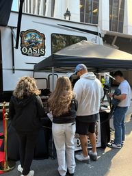 Four people at a mobile cigar lounge booth under a black canopy beside a white trailer on a downtown city street, outdoor event vibe
